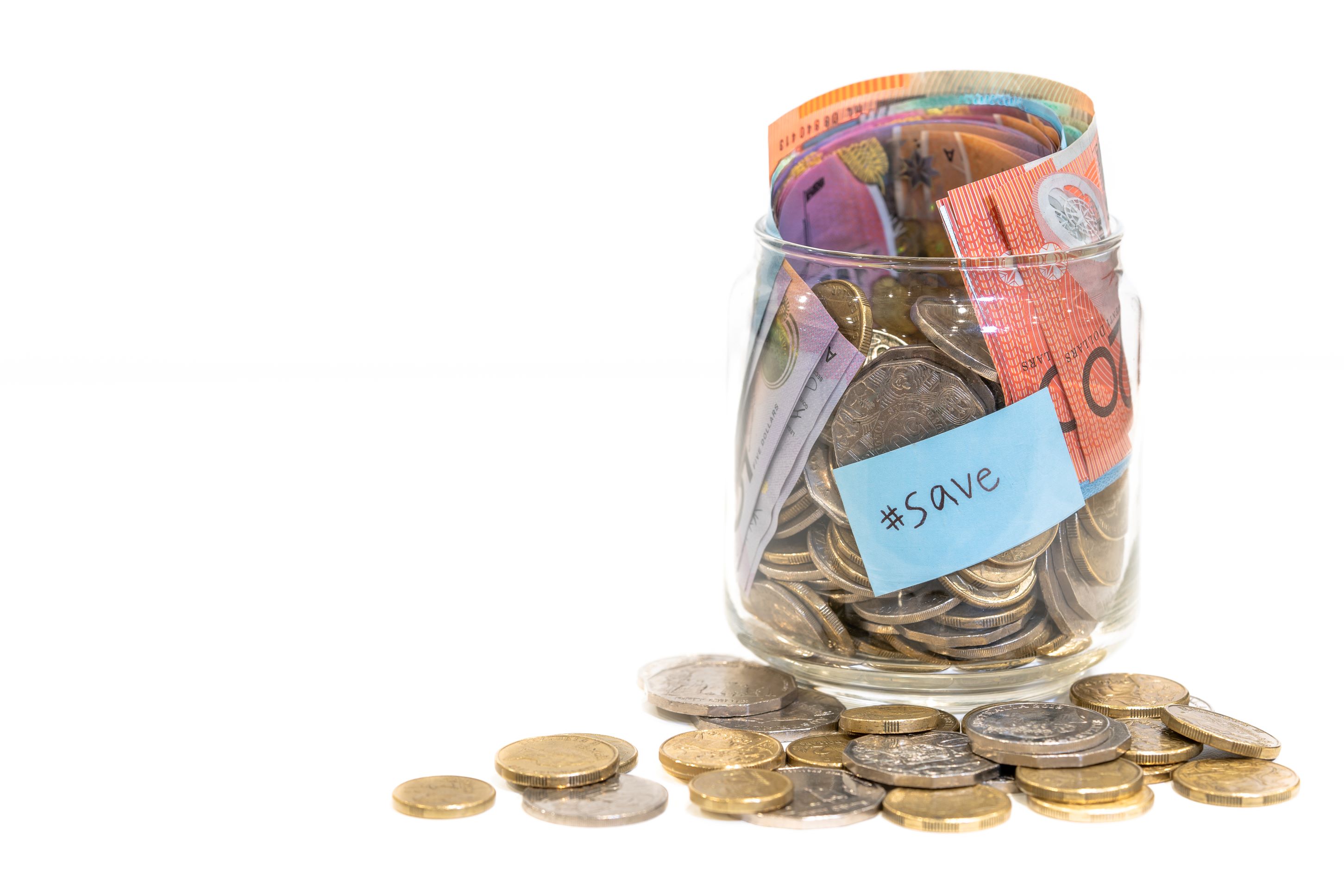 A glass jar filled with cash, both coins and notes, with coins spilled around it