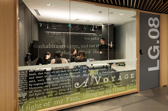 Group of students discussing topic around a large table in a room with a glass wall