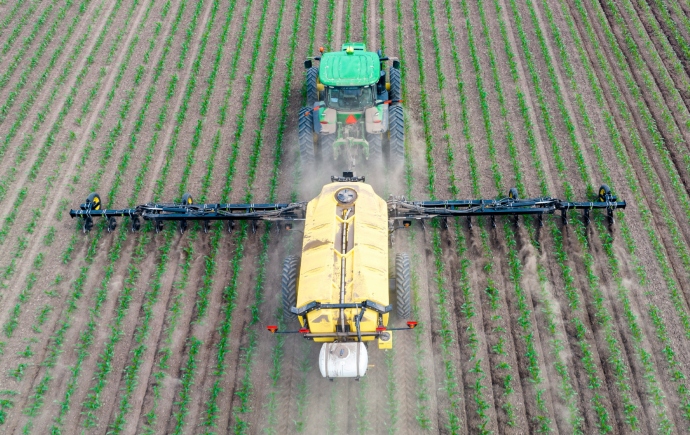 A green tractor spraying crops in an agricultural field.