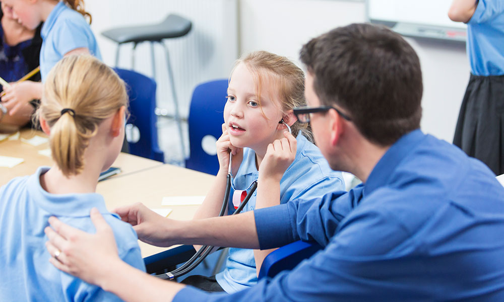 A school student measuring a heart beat of another student in a classroom