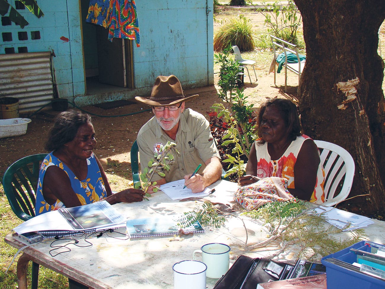 Nikipini Dalak Glenn Wightman and Lily Bennett sitting at a table writing on paper