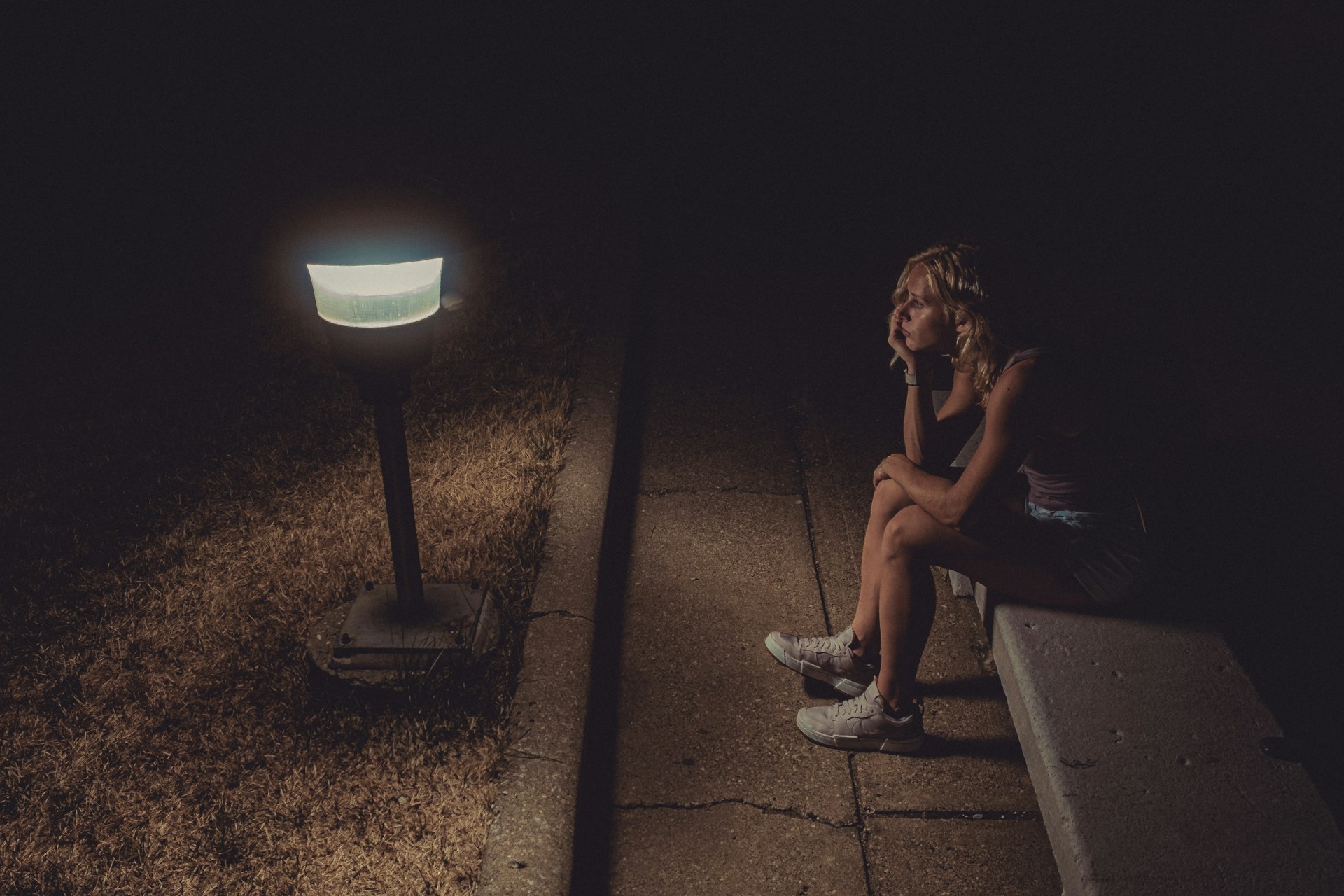 Woman in black tank top sitting on concrete floor.