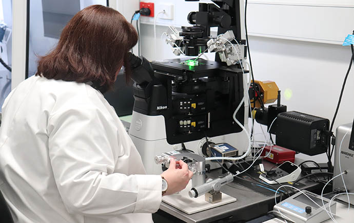 Clinical embryologist Mel wears a lab coat while looking into a microscope in the lab