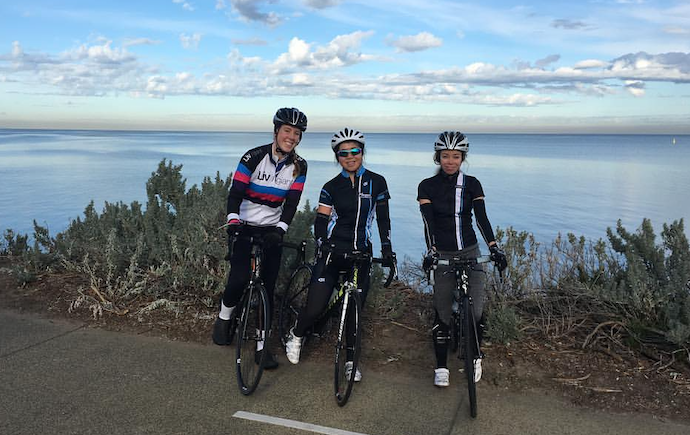 3 triathlon participants posing with bikes in front of ocean