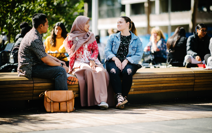 Three people sitting outside Monash Matheson Library on bench 