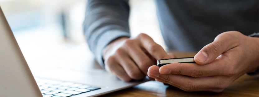 hands holding mobile device with laptop