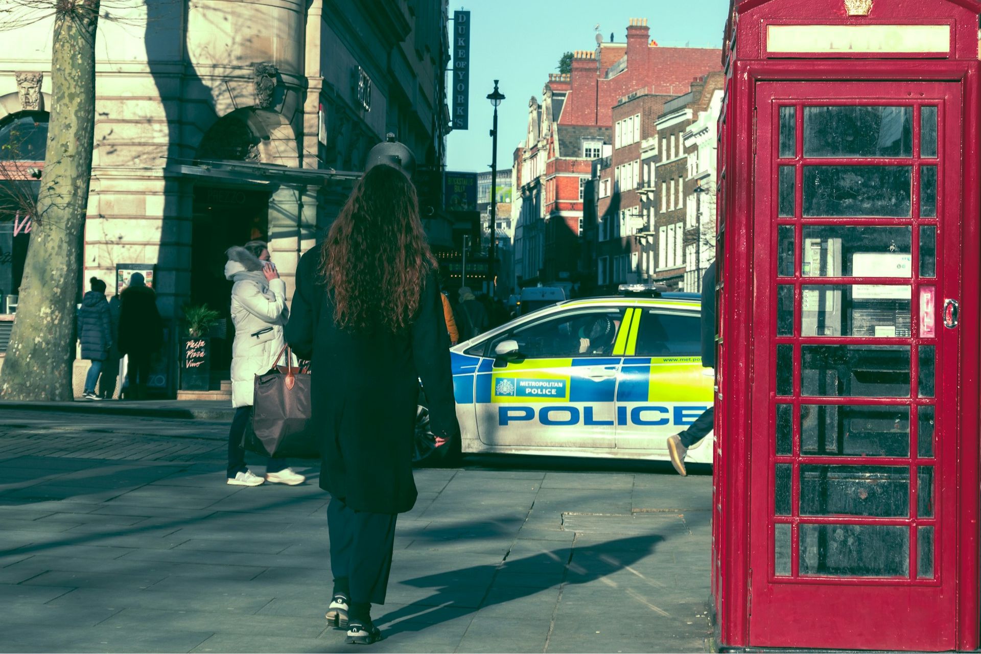 A woman walking down a London street next to a police car.