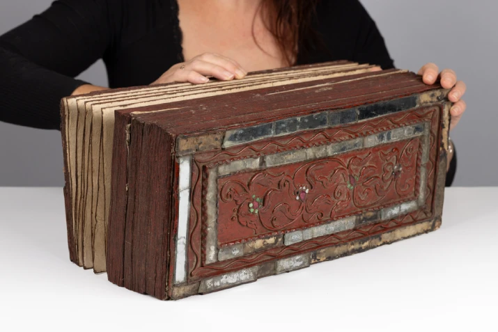 An accordion-like book, the pages folded closed together and resting on a table