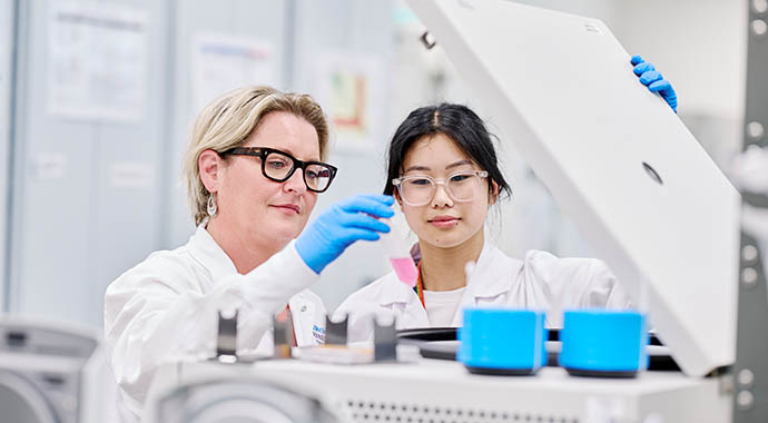 Two female researchers removing a fluid fro a cold storage container.