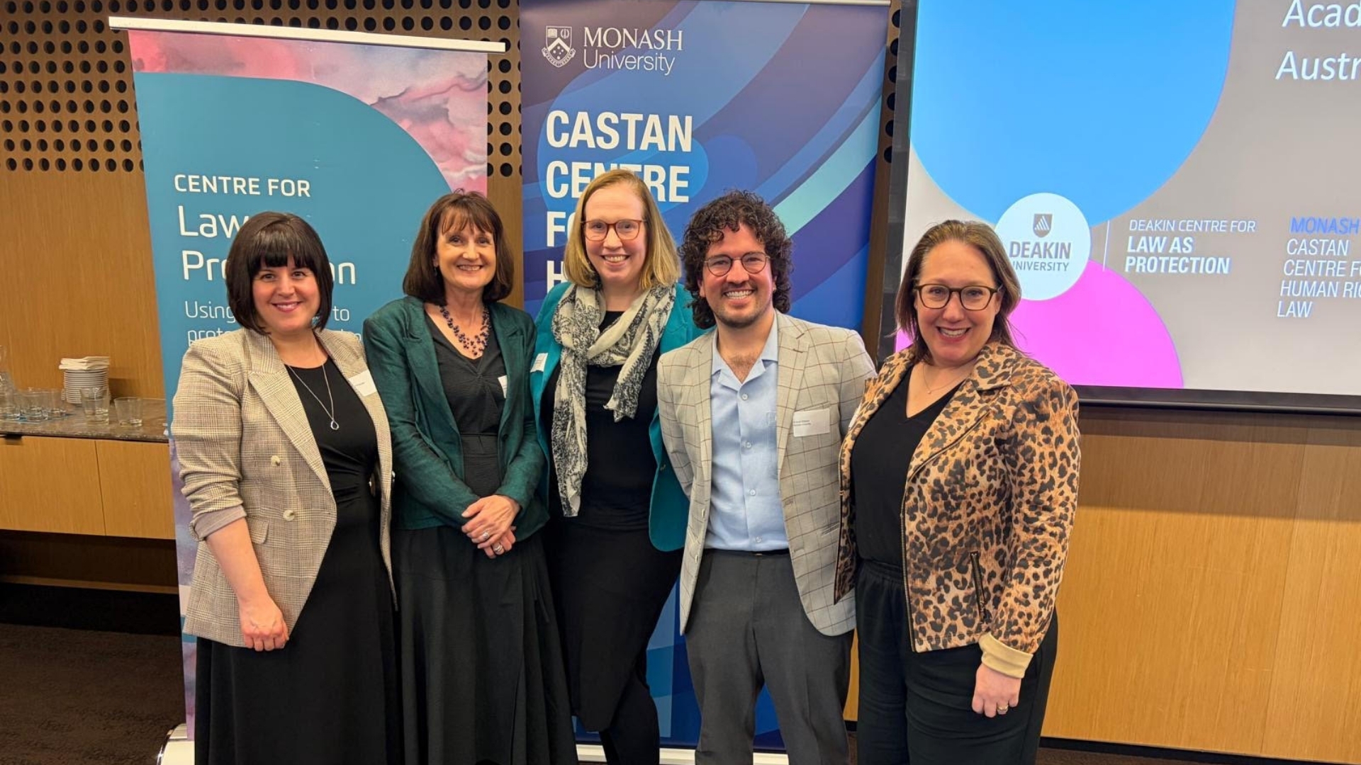 Tanya Josev, Tania Penovic, Anne Carter, Josh Gibson, and Ronli Sifris smiling in front of the Castan Centre banner.