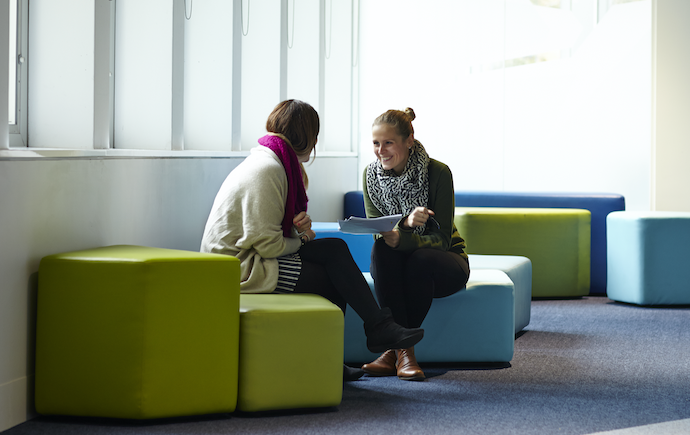 Two women speaking on couches located within Monash Clayton campus menzies building