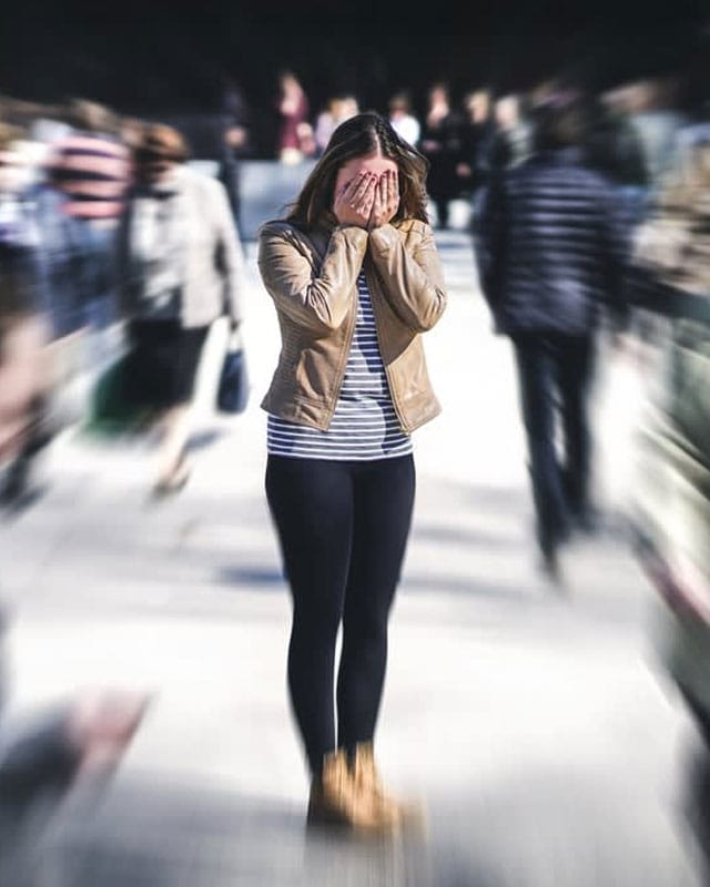 woman standing in a blurry crowd with her hands over face