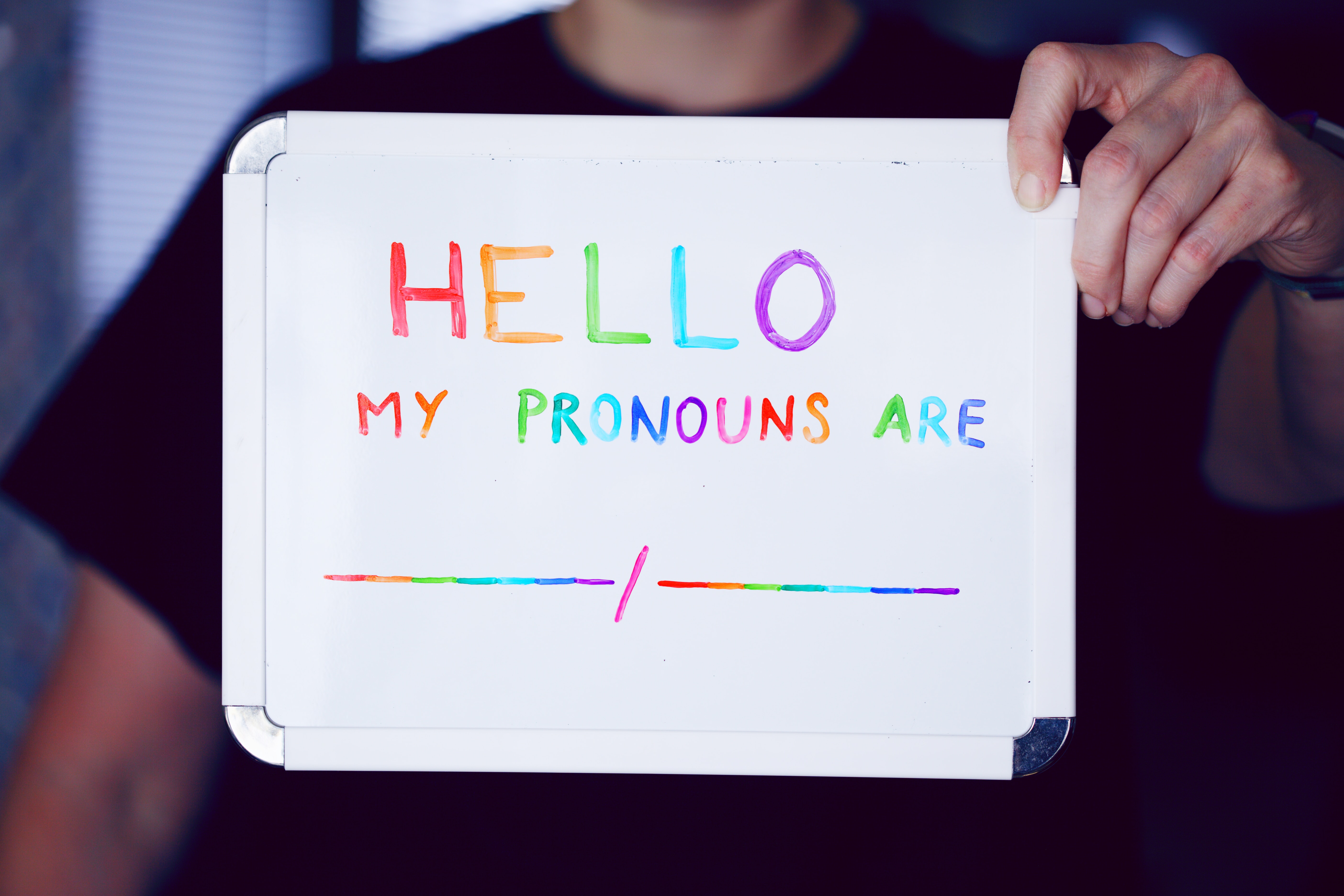 Person holding a whiteboard saying Hello My Pronouns are ...