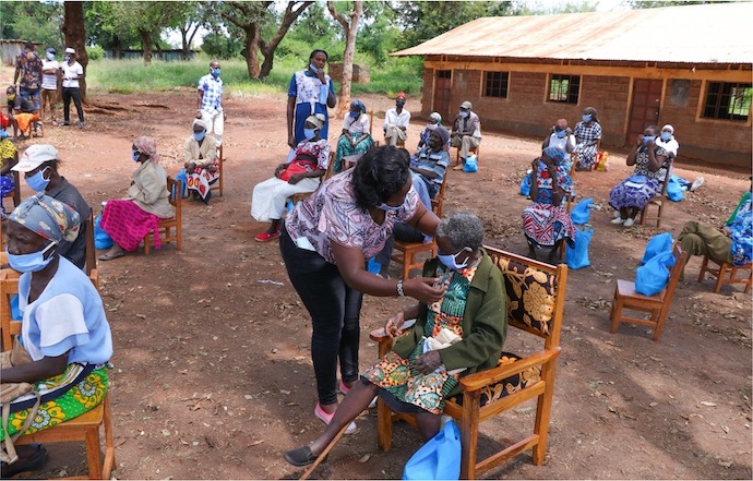 Elderly people sitting on chairs in yard of hospital in an African village