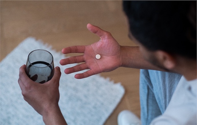 Man holding a white pill in one hand and a glass of water in another