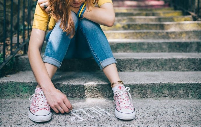 Young person writing 'help' on pavement