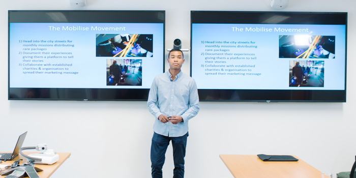 noah yang standing in front of two screens with presentations