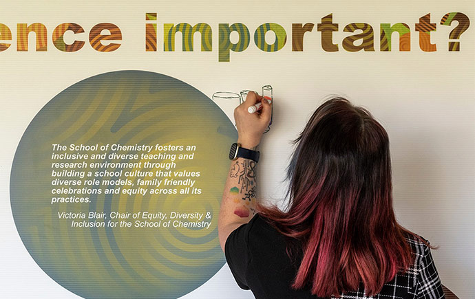 Student draws on wall poster beside a quote by Victoria Blair, Chair of Equity, Diversity & Inclusion for the School of Chemistry