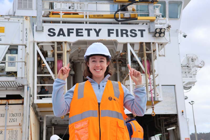 Amelia Pearson standing on RV Investigator deck pointing upwards at safety first sign