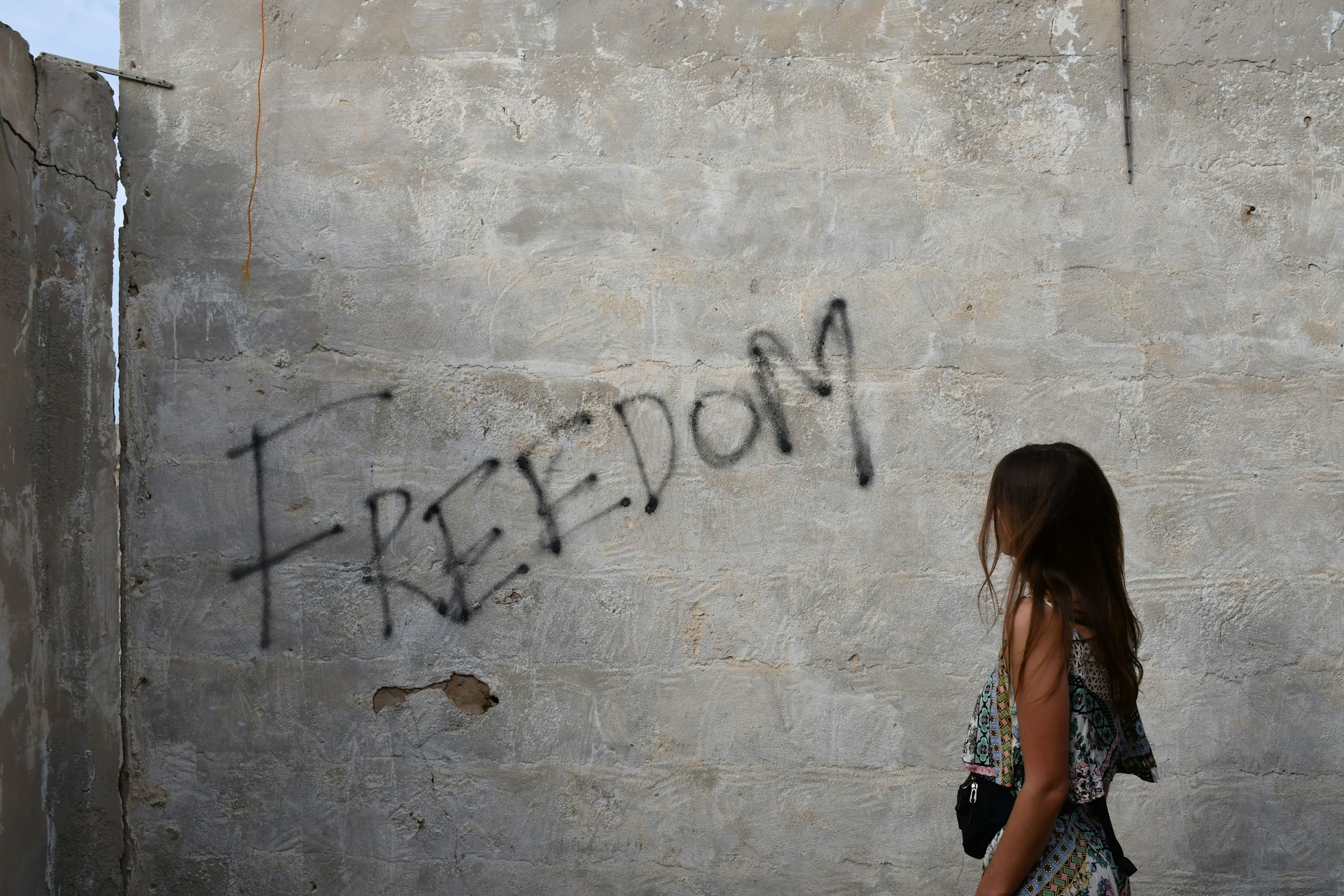 Woman leaning on a wall with the word freedom.
