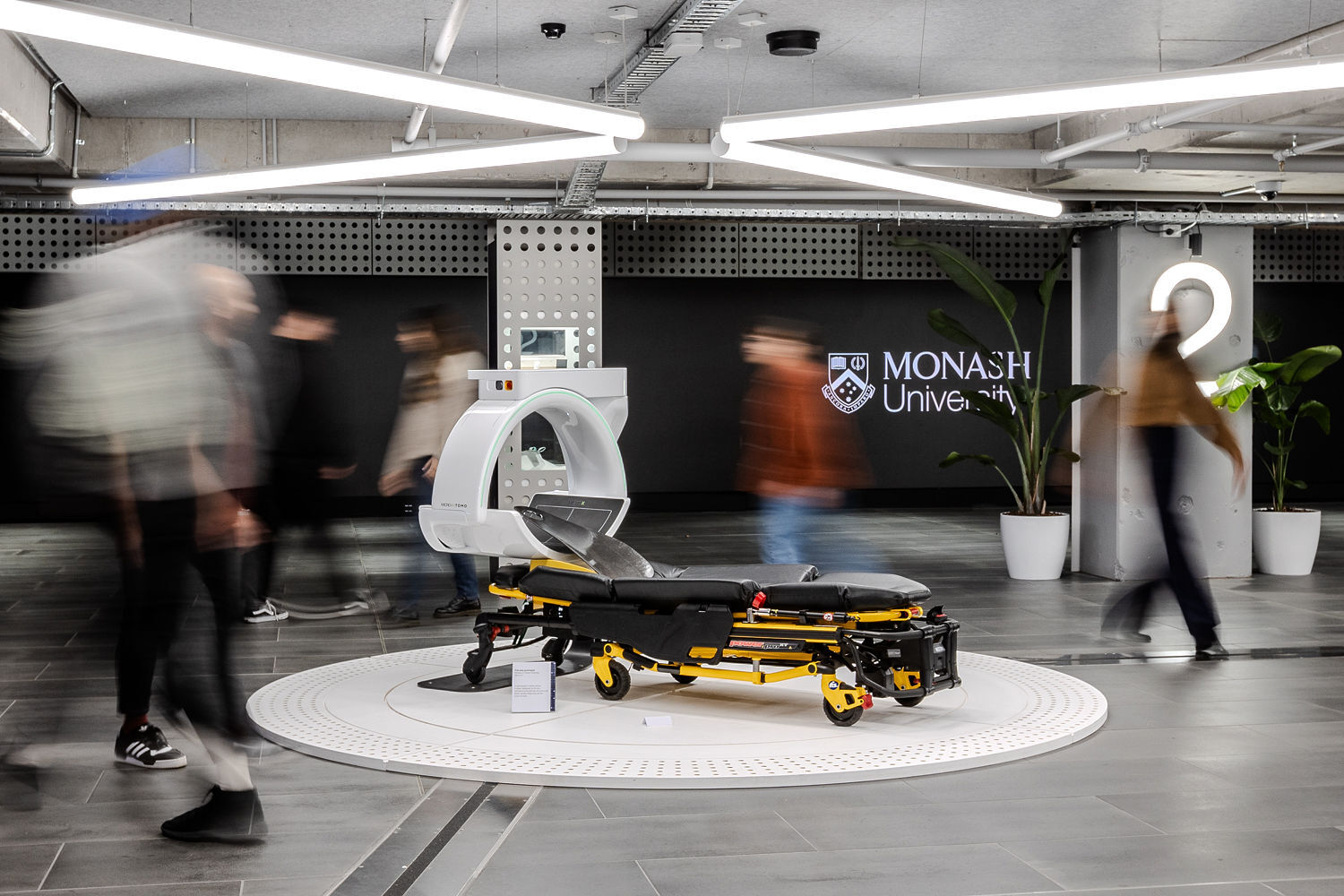 People walking past a CT-scanning medical gurney.