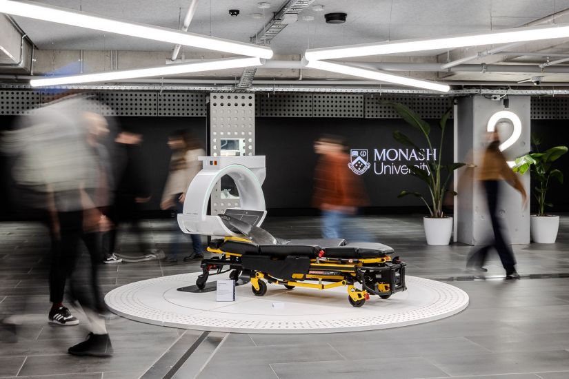 People walking past a CT-scanning medical gurney.