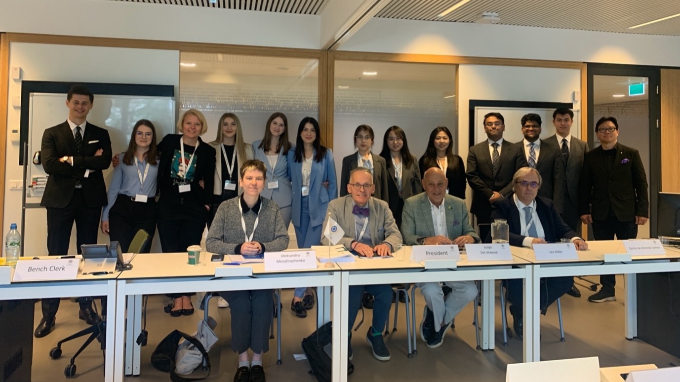 L to R (seated) are panel judges, Oleksandra Miroshnychenko, USA Judge Del Atwood, Leo Atwood, Carlos de Almeida Lemos. Standing are the 3 teams representing Defence, Victim, and Prosecution including their coaches