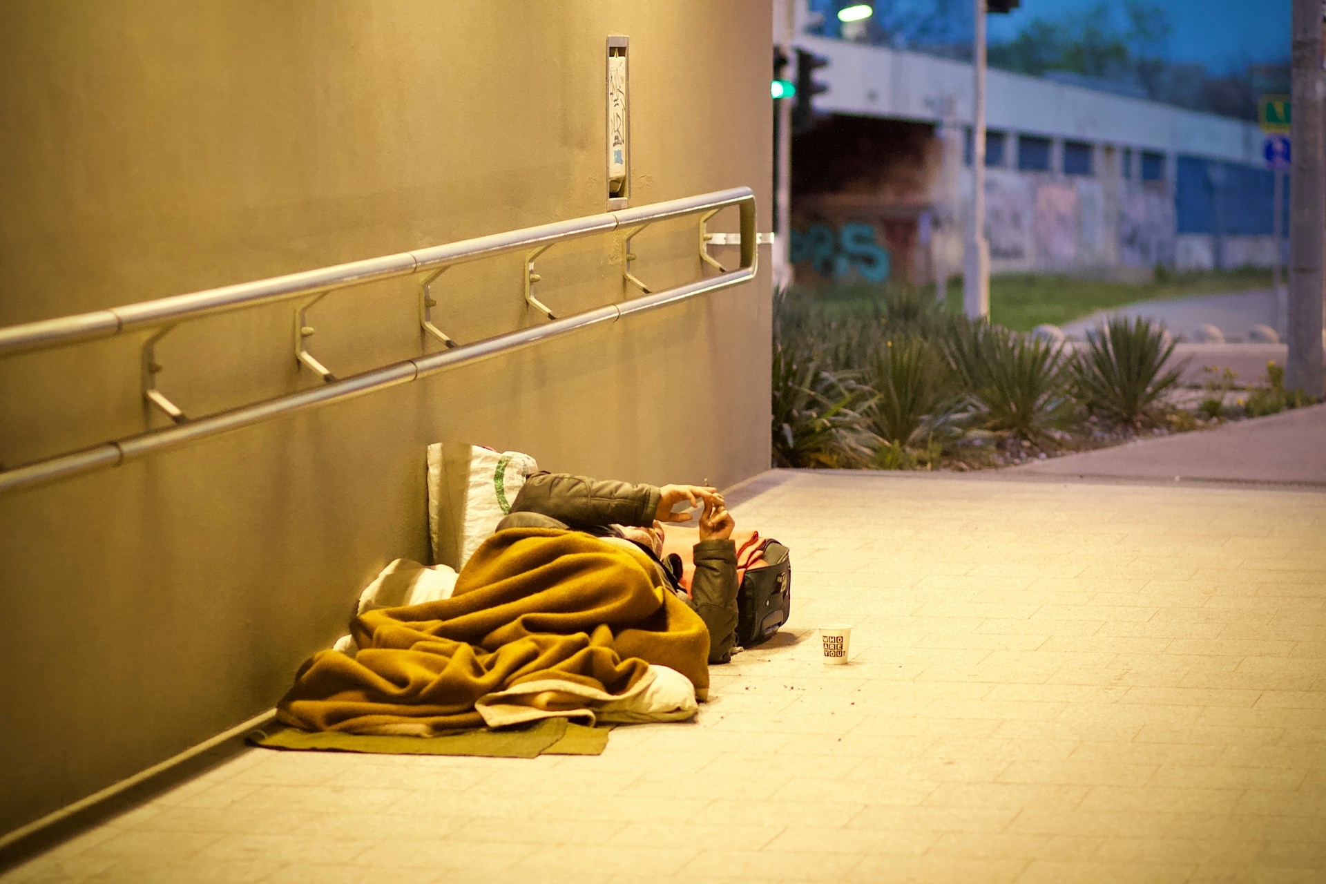 A homeless person in a pedestrian walkway at night, laying under blankets.