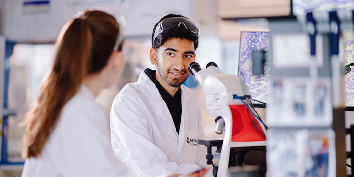 Two researchers in a lab, conversing next to a microscope.