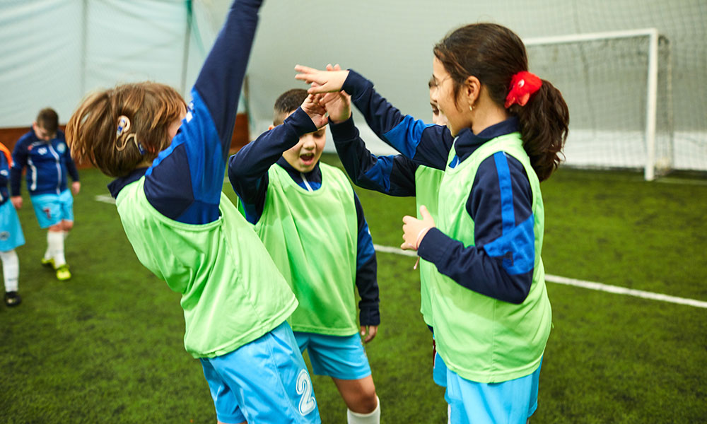 Girl with a hearing aid is among the kids giving each other hi five at the end of soccer game