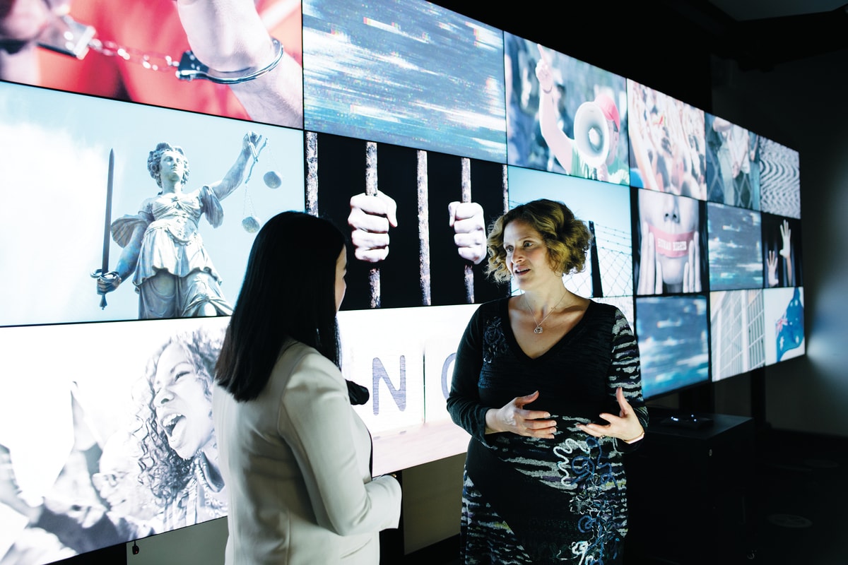 Sara Kowal talking to another person in front of wall of screens