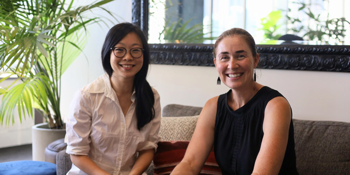 Kun Zhao and Beth Eggleston on a couch next to a plant