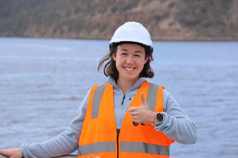 Amelia Pearson with a thumb up on deck of RV Investigator with ocean as background