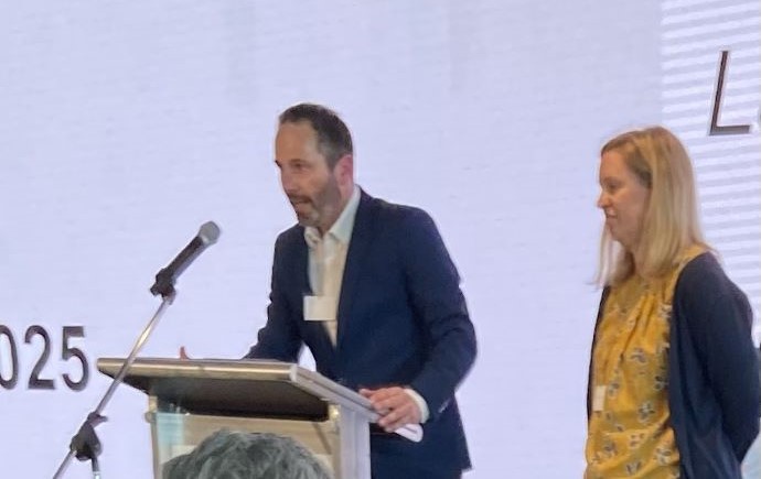 Damian Dowling speaking at a podium with Ailie Gallant