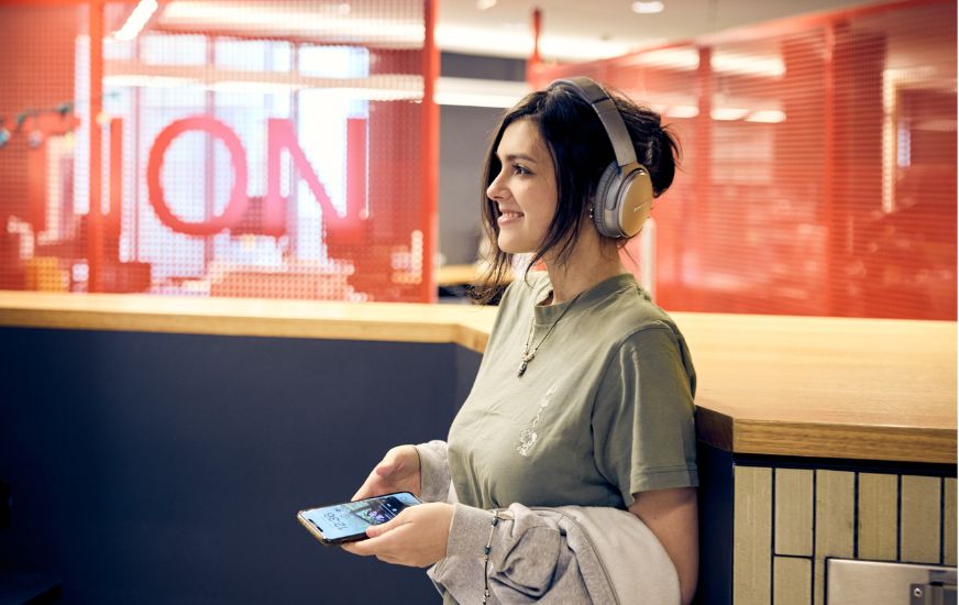 Student wearing headphones, holding a phone at the Library information point