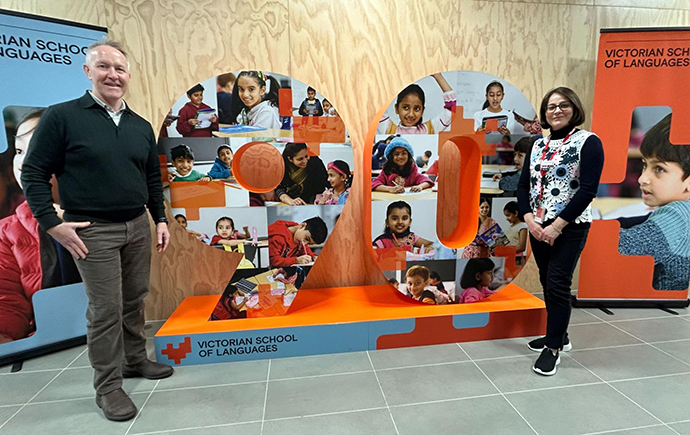 Two people standing beside a large &ldquo;90&rdquo; display featuring photos of students.