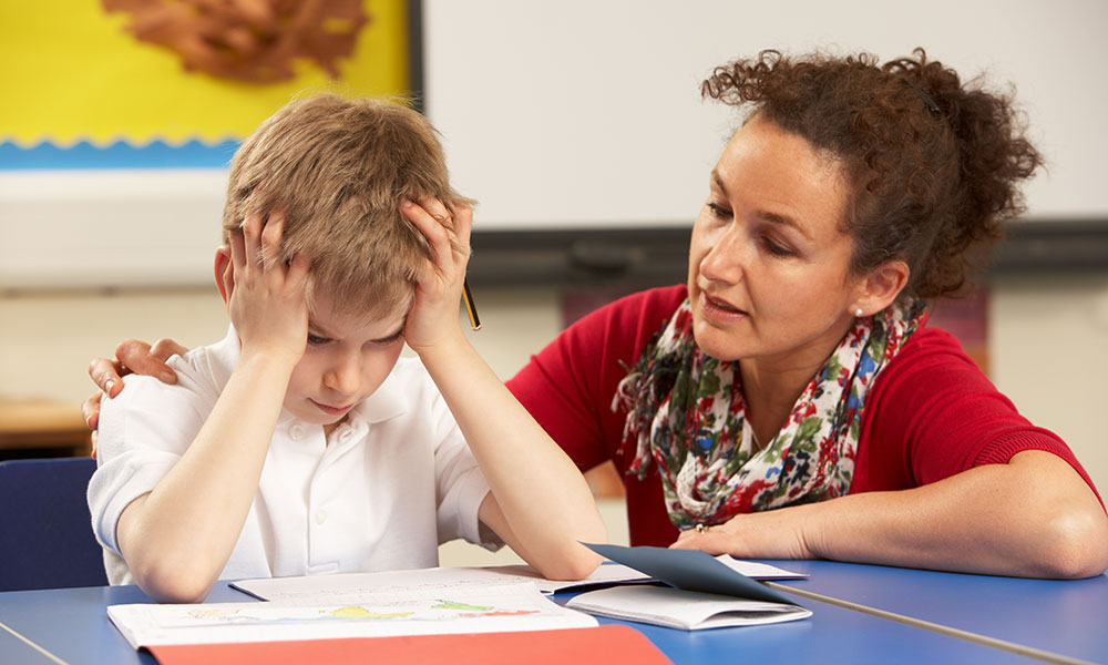 boy sitting at a desk trying to study and he is holding a sign that reads 'help