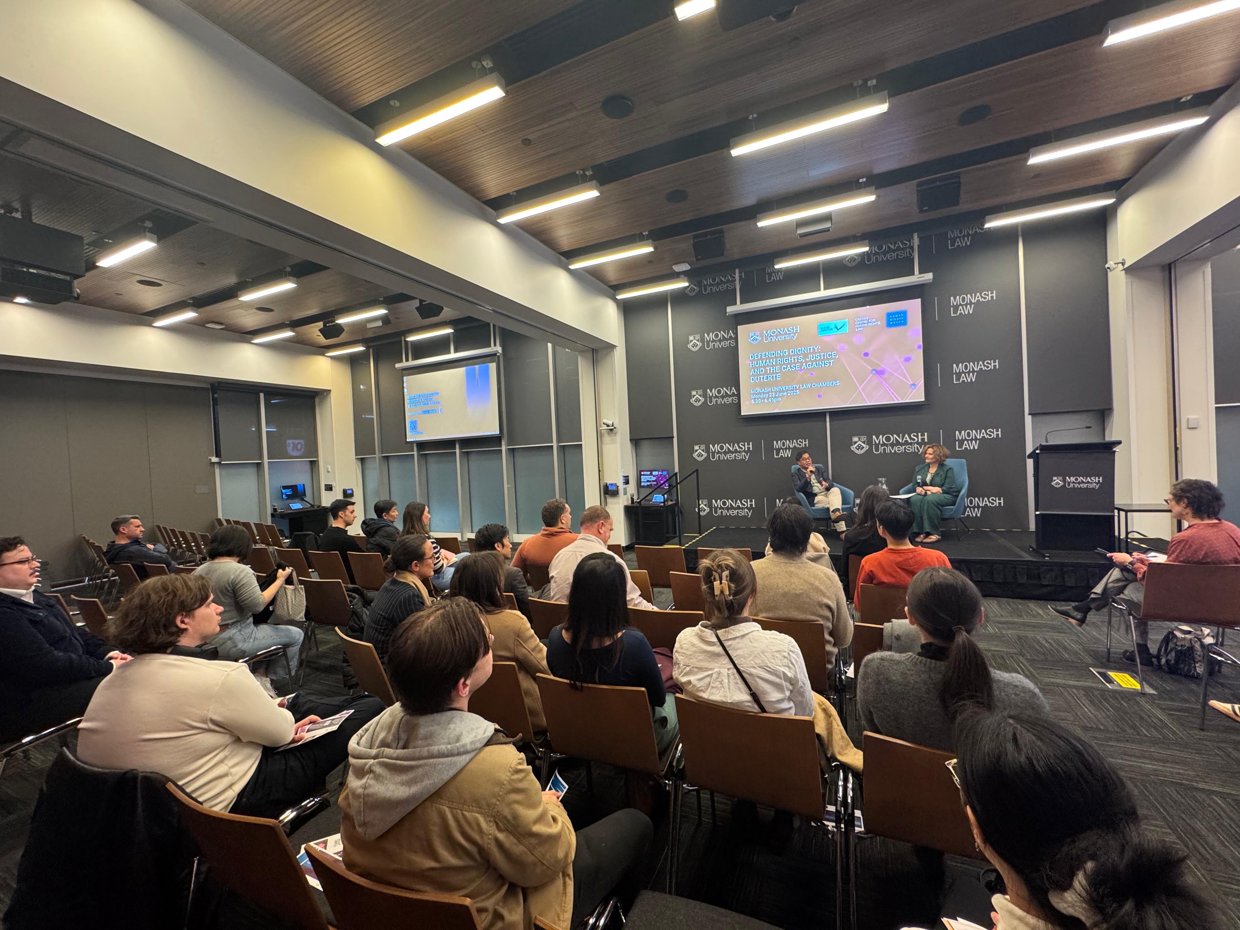 Carlos H. Conde and Sara Kowal speaking on stage from an audience perspective.