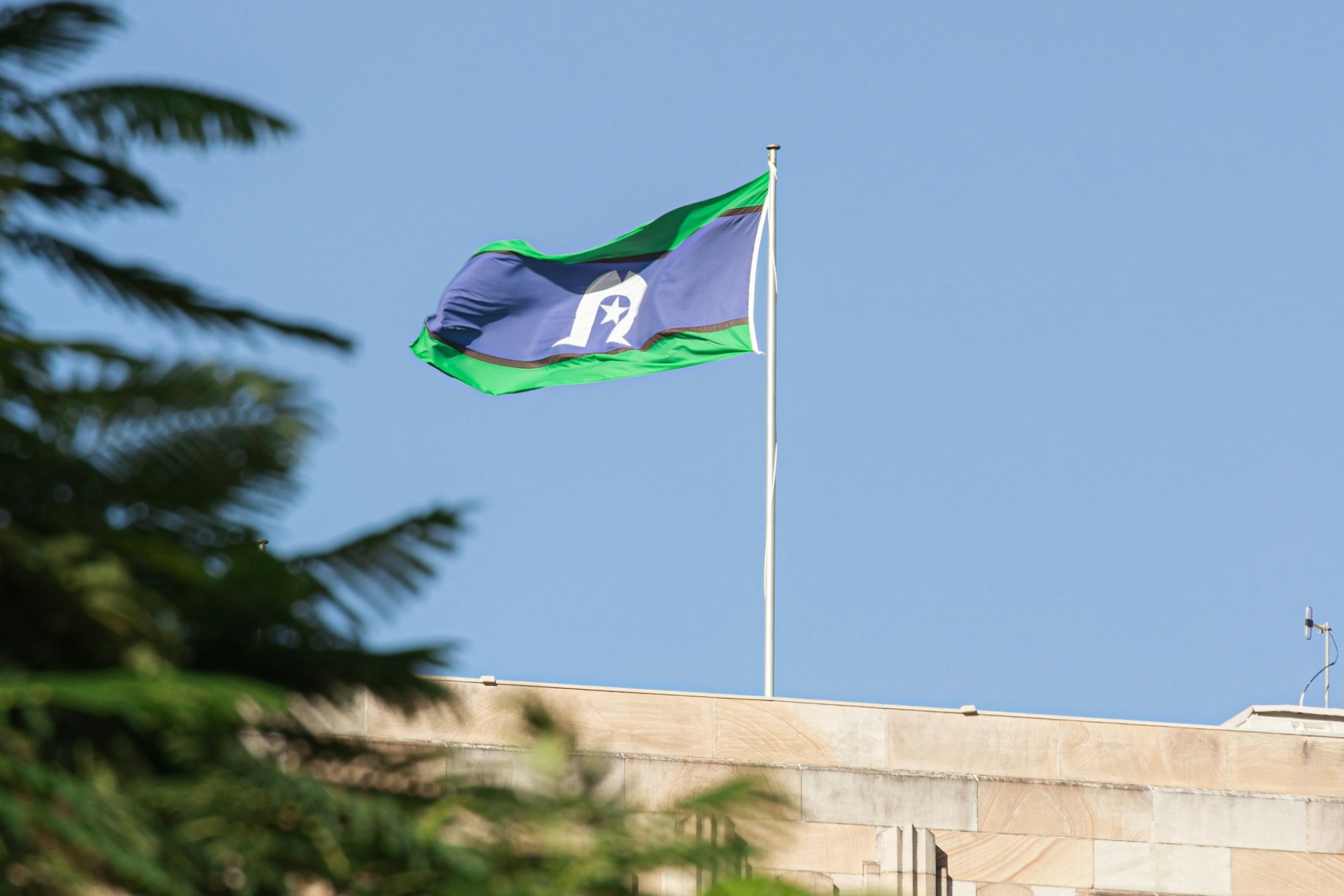 A photo of the Torres Strait Islander flag flying on top of a building.