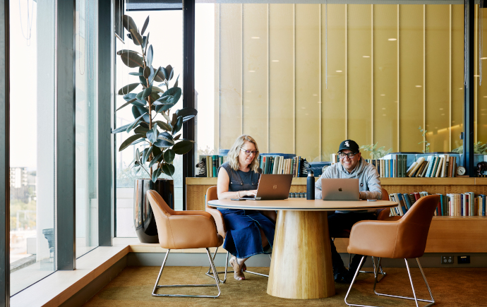 Two postgraduate students sitting at table with laptops  