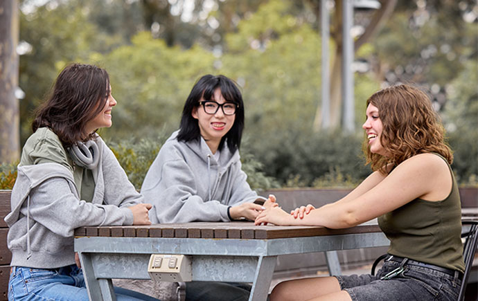 Three students sitting at a table outdoors on campus