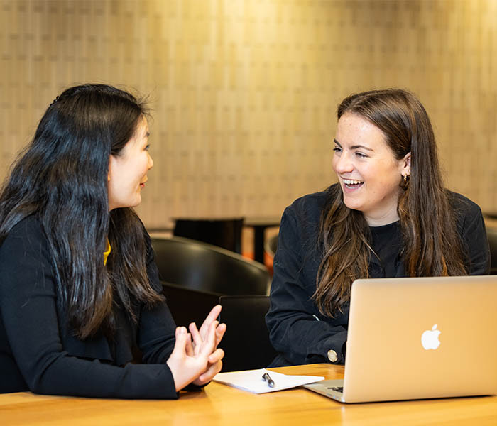 Two students smiling and talking to each other.