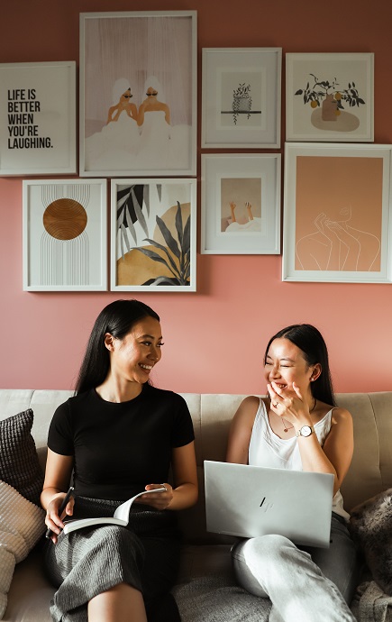 Estefania Tchung and Elizabeth Le sitting on a couch with laptops and laughing