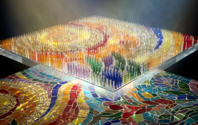 Colorful glass-like rods form a raised, square mosaic panel illuminated from below, displaying swirling abstract patterns. The panel hovers above a multicolored mosaic surface, with warm light beams shining upward and highlighting the vibrant