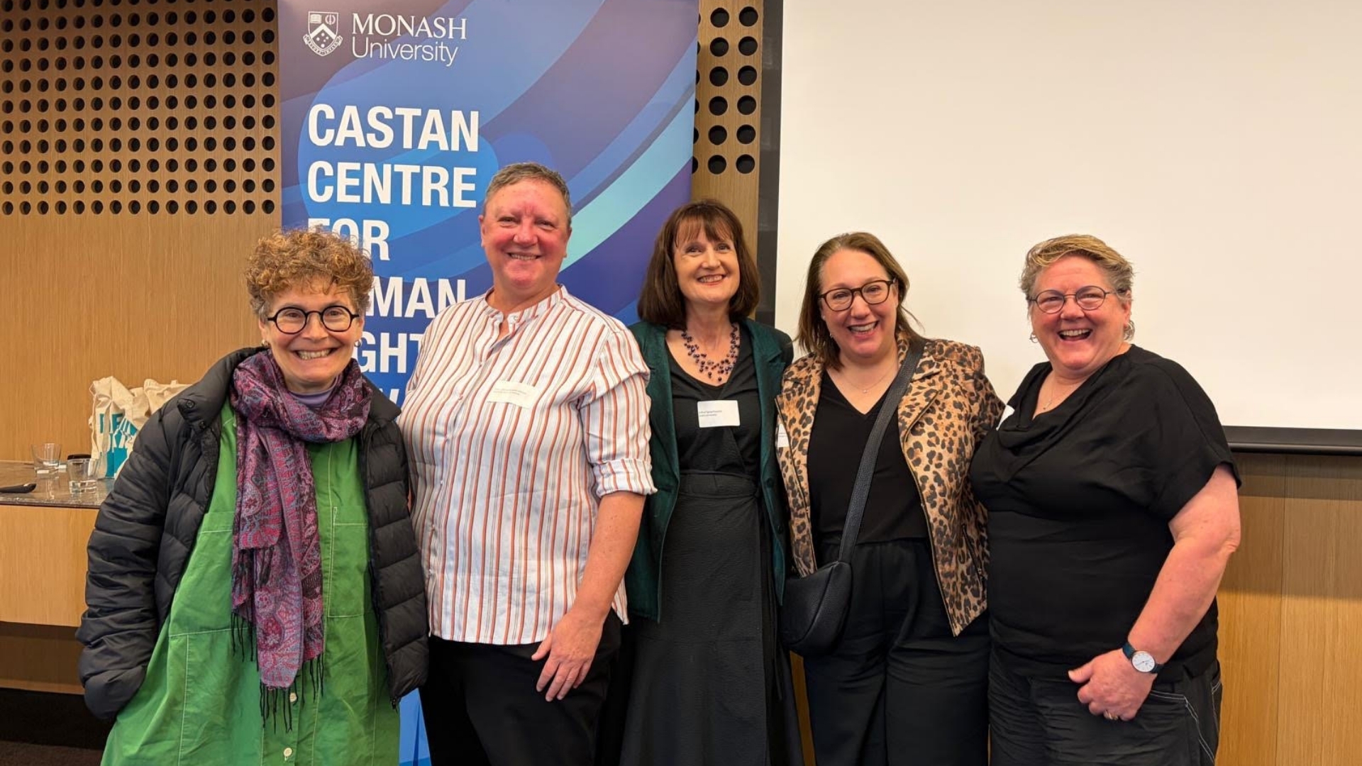 Kim Rubenstein, Kristen Walker, Tania Penovic, Ronli Sifris, and Paula Gerber standing smiling near the Castan Centre banner.